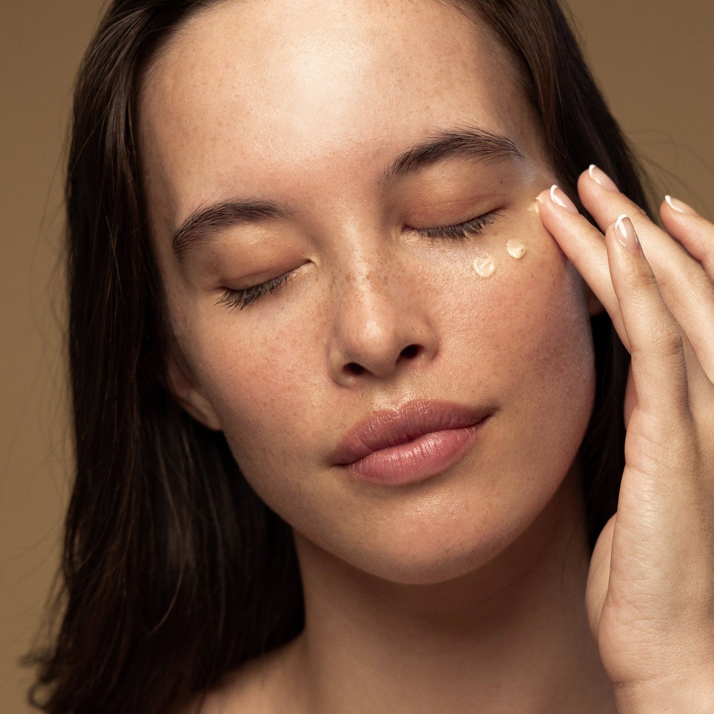A woman applies Antipodes Kiwi Seed 23K Gold Luminous Eye Cream on the skin around eyes