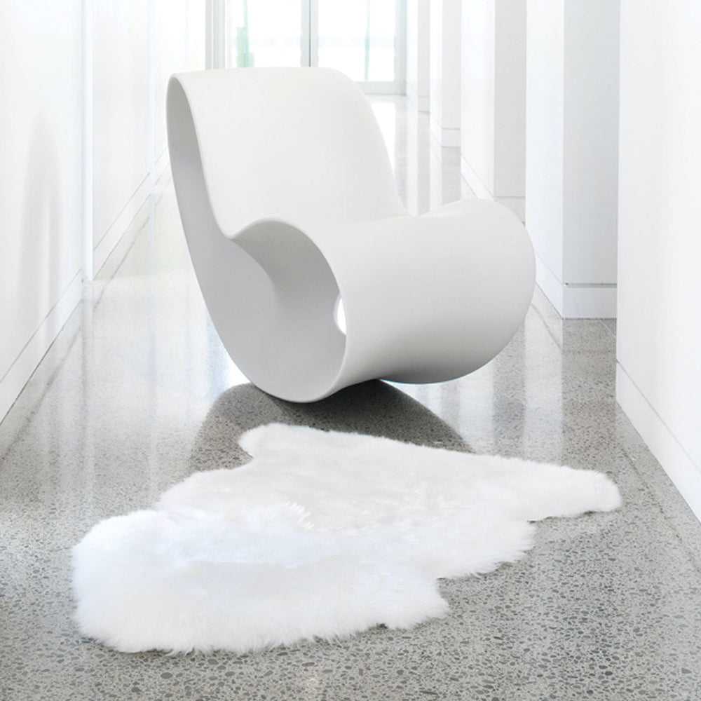A single rectangular New Zealand sheepskin rug in ivory color, displayed on a floor, with a modern chair in the background.