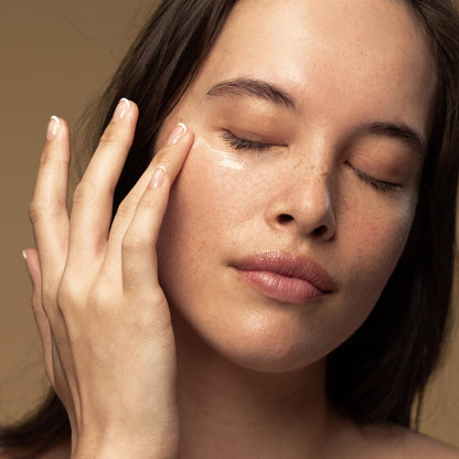 A woman applies Antipodes Kiwi Seed Oil Eye Cream on her face