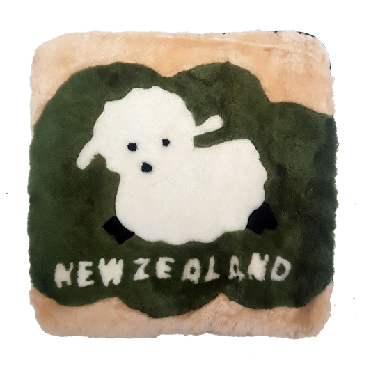 A square-shaped cushion with a green background featuring a white baby lamb on top of a grass-like pattern. The cushion also has the text 'NEW ZEALAND' at the bottom.