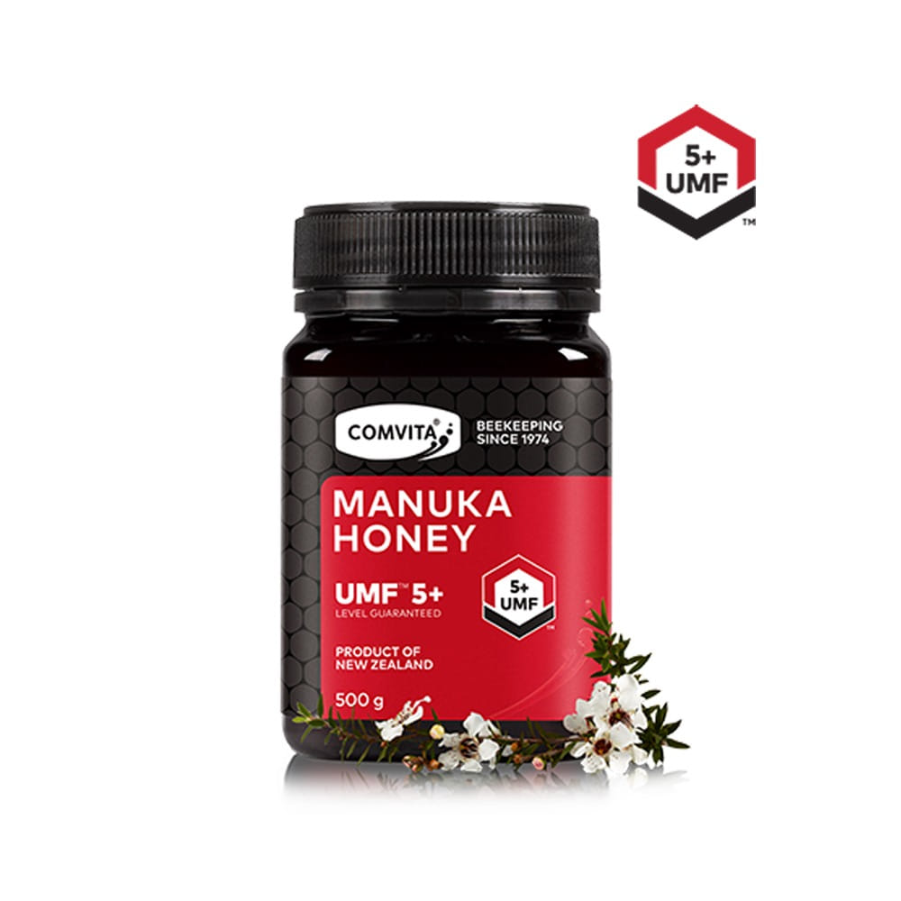 A jar of Comvita UMF 5+ Manuka Honey, with a red label and a clear window showing the honey's color and texture. The product is presented with a background of flowers, indicating its natural qualities.